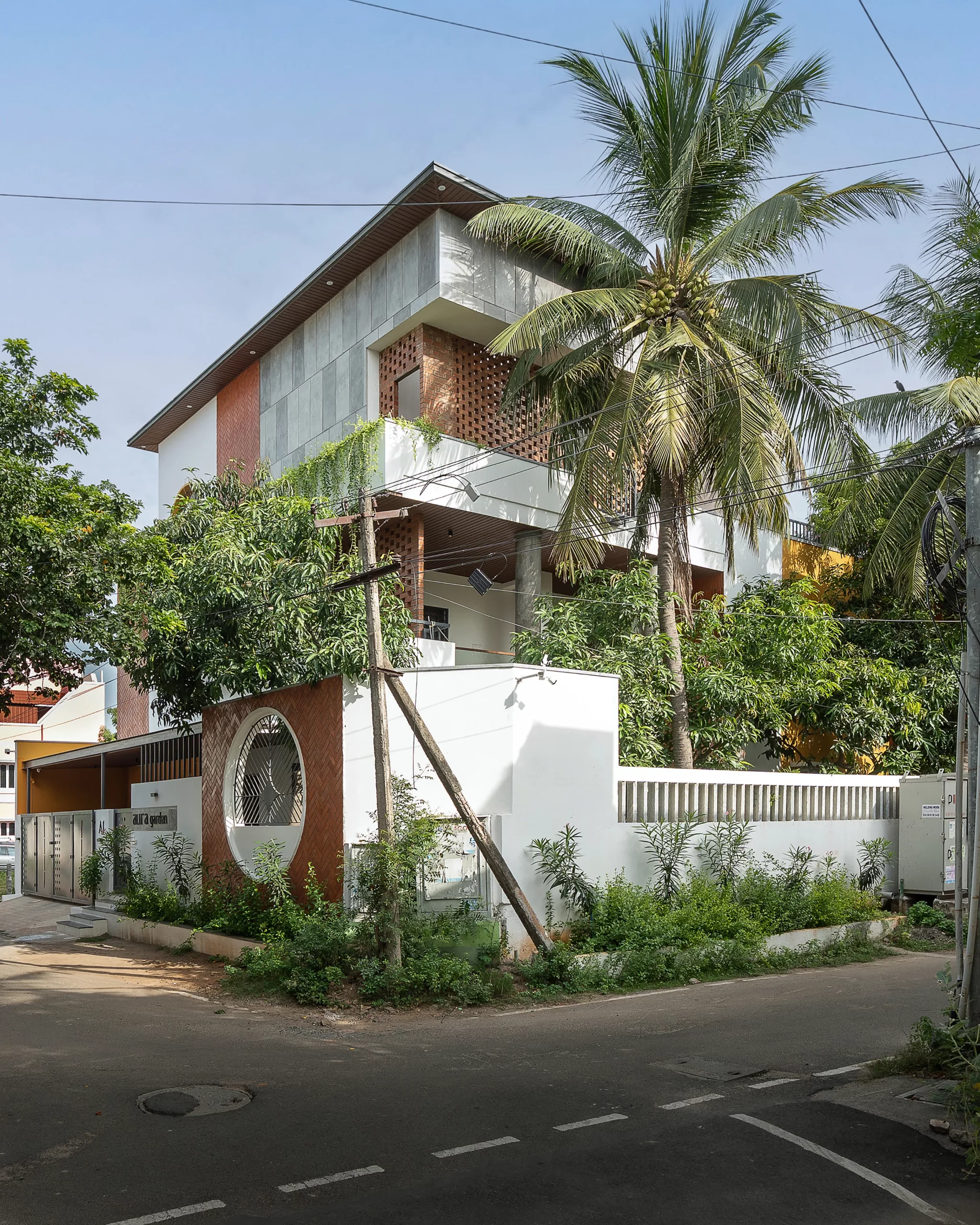 The house from the south-east corner, with terracotta jaali screens on the upper floor, coconut palms and a white garden wall